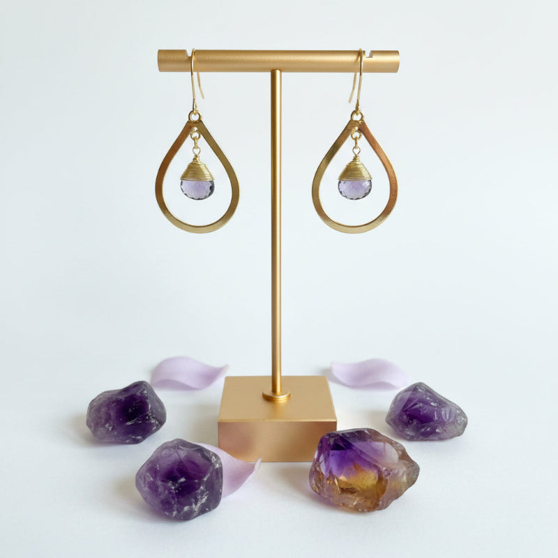 Close-up of gold bold teardrop earring with wire-wrapped faceted amethyst drop