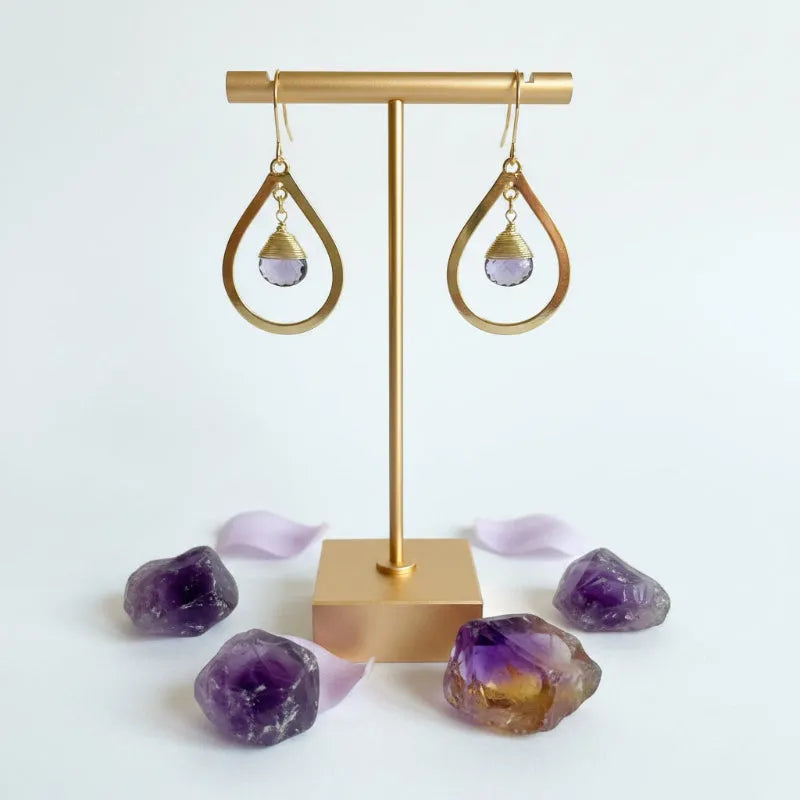 Close-up of gold bold teardrop earring with wire-wrapped faceted amethyst drop