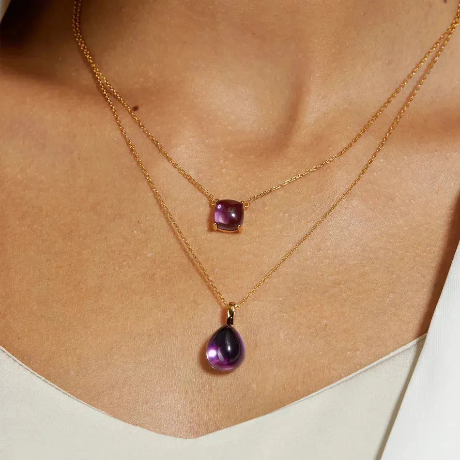 Two gold necklaces with purple gemstones on a person's neck.