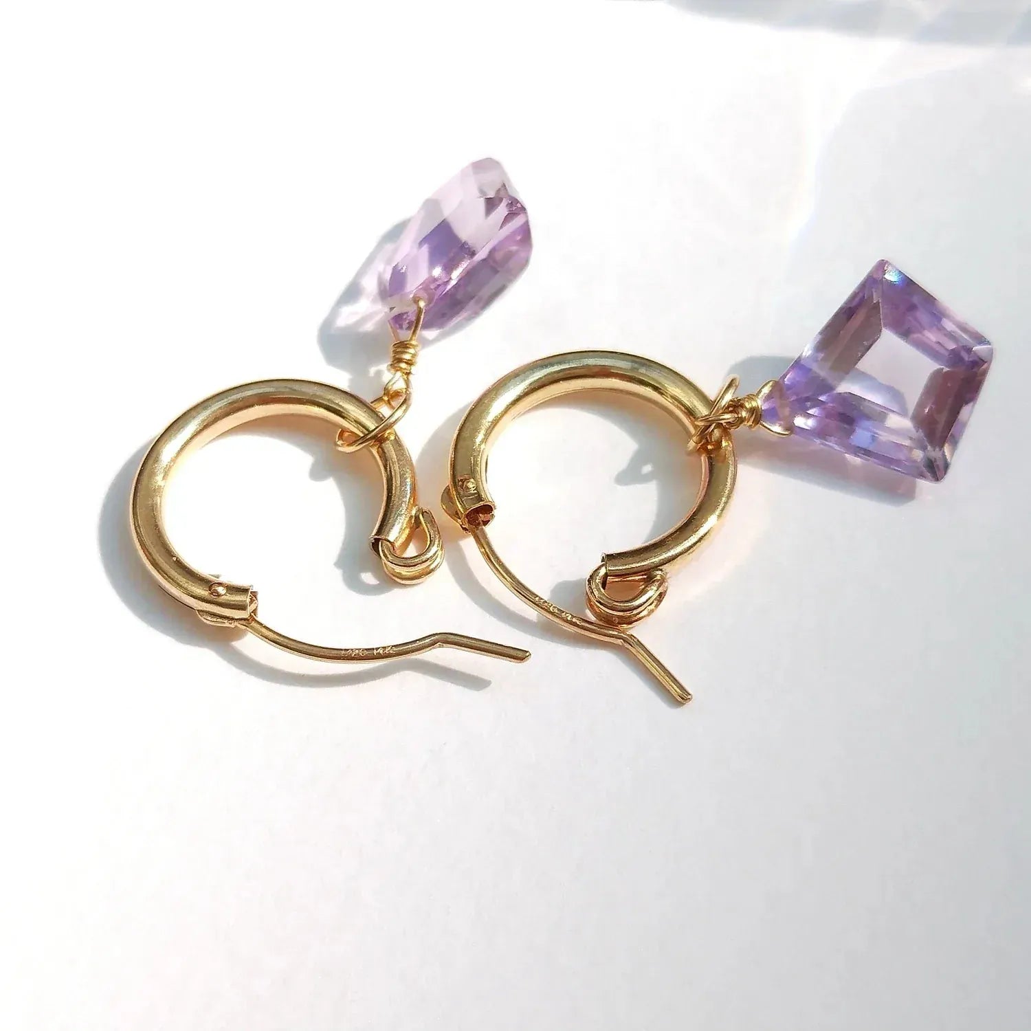 Gold hoop earrings with purple crystal accents on a white background