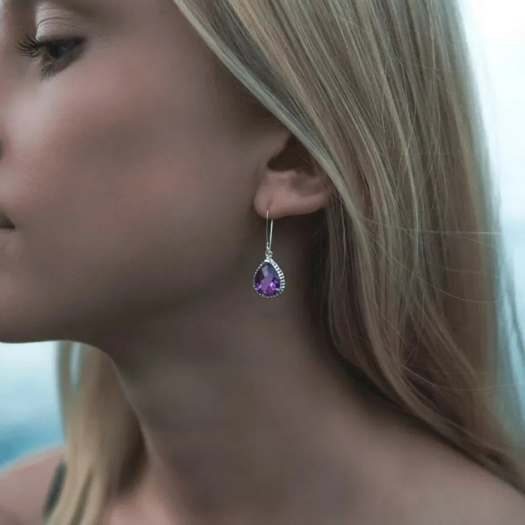 Close-up of a woman wearing a teardrop earring with a purple gemstone.
