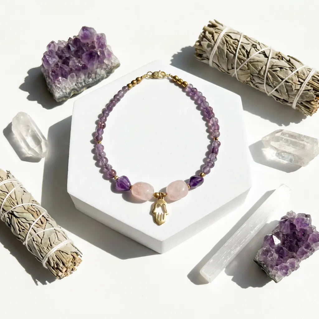 Purple beaded bracelet with gold charm on a white stand, surrounded by crystals and smudge sticks.