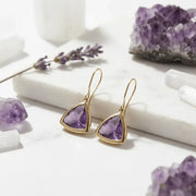 Gold earrings with purple gemstones on a white surface with amethyst stones and lavender.