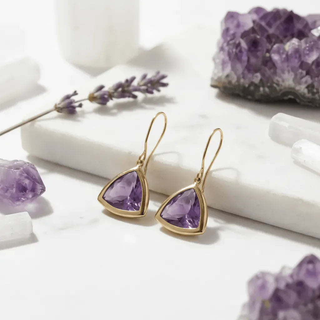 Gold earrings with purple gemstones on a white surface with amethyst stones and lavender.