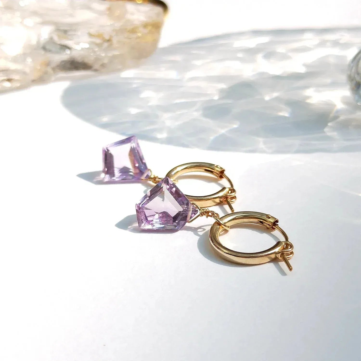 Gold hoop earrings with pink gemstones on a white surface