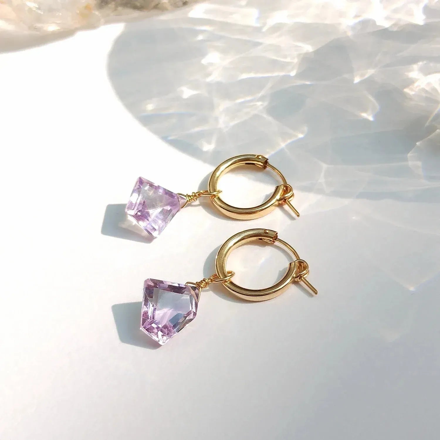 Gold hoop earrings with pink gemstones on a white background