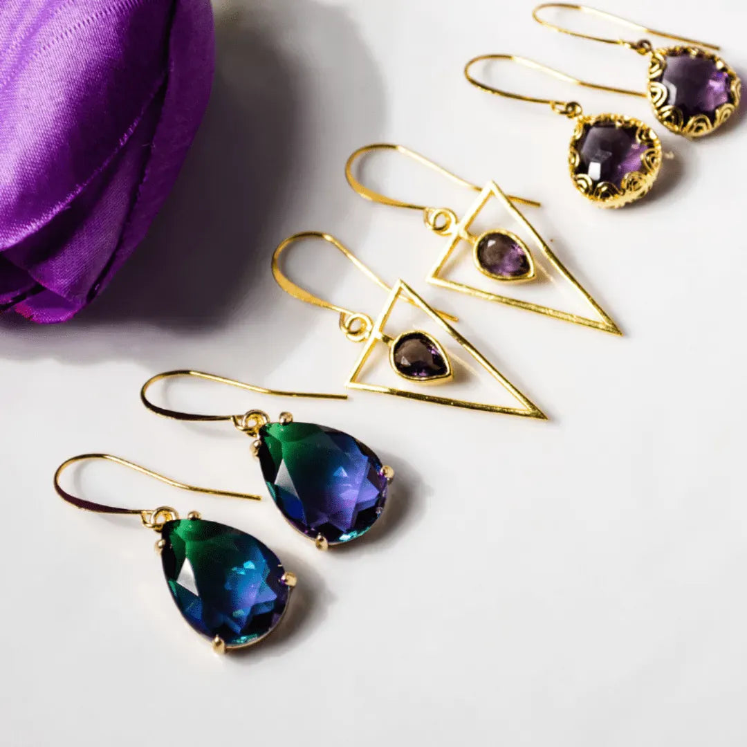 Gold earrings with purple and green gemstones on a white surface.