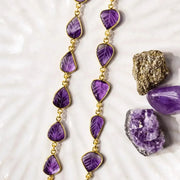 Purple gemstone necklace on a textured white surface with amethyst stones.