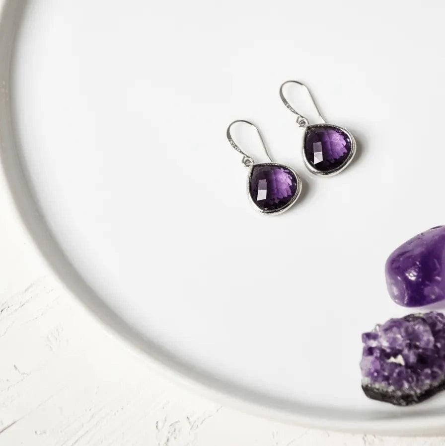 Purple teardrop earrings on a white surface with amethyst stones.