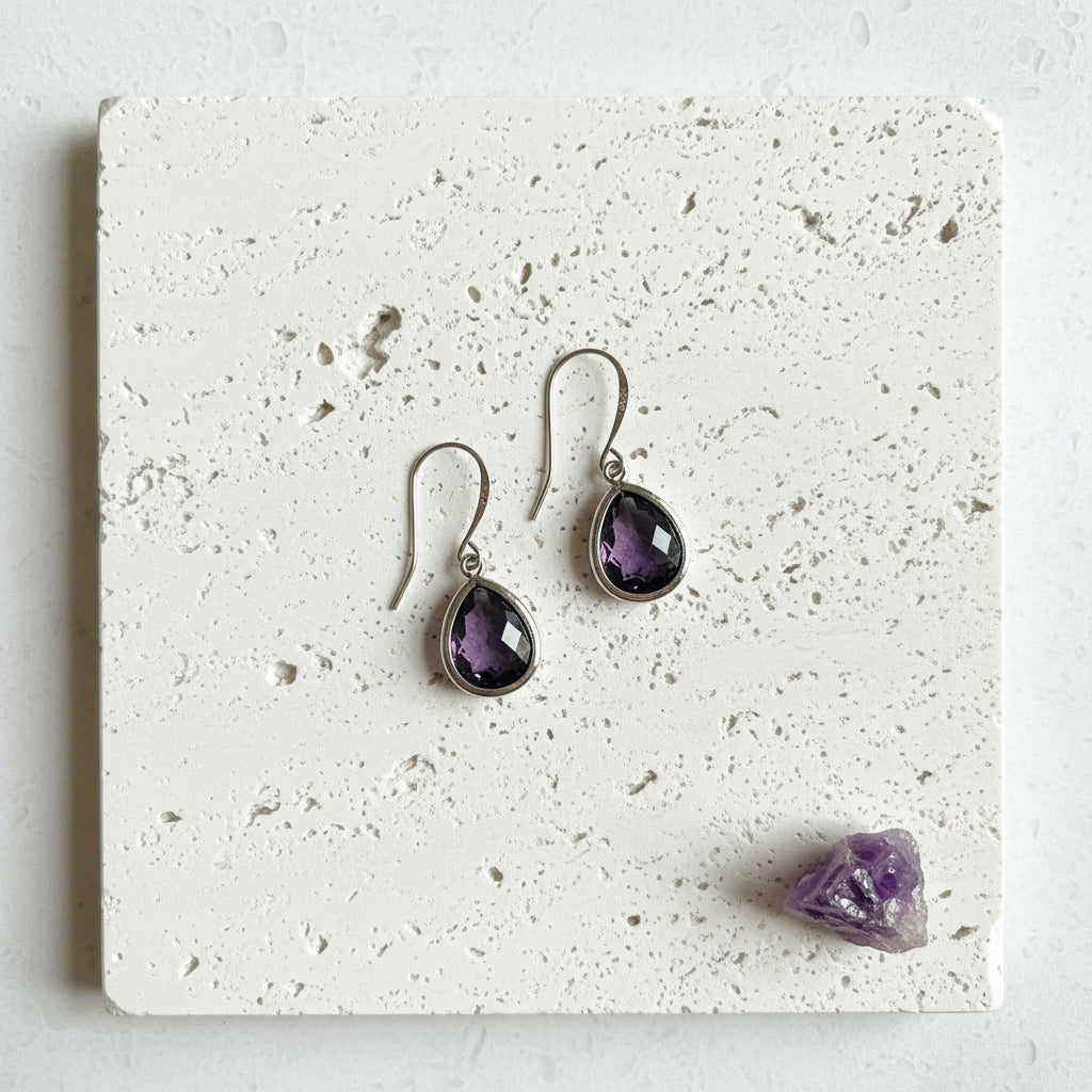 Amethyst purple faceted glass drop earrings in silver plated brass, pair laid flat