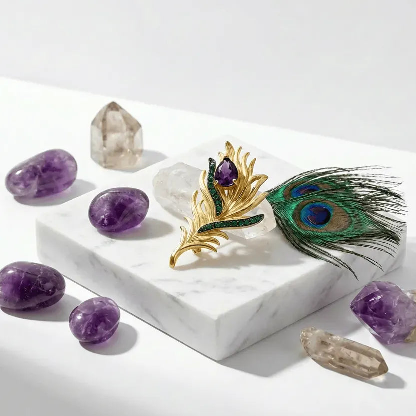 Decorative display with amethyst crystals, a gold brooch, and a peacock feather on a white marble surface.