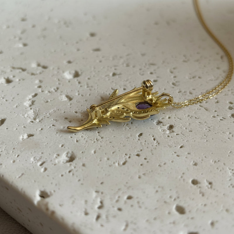 Gold amethyst peacock feather pin and pendant on a peacock feather background