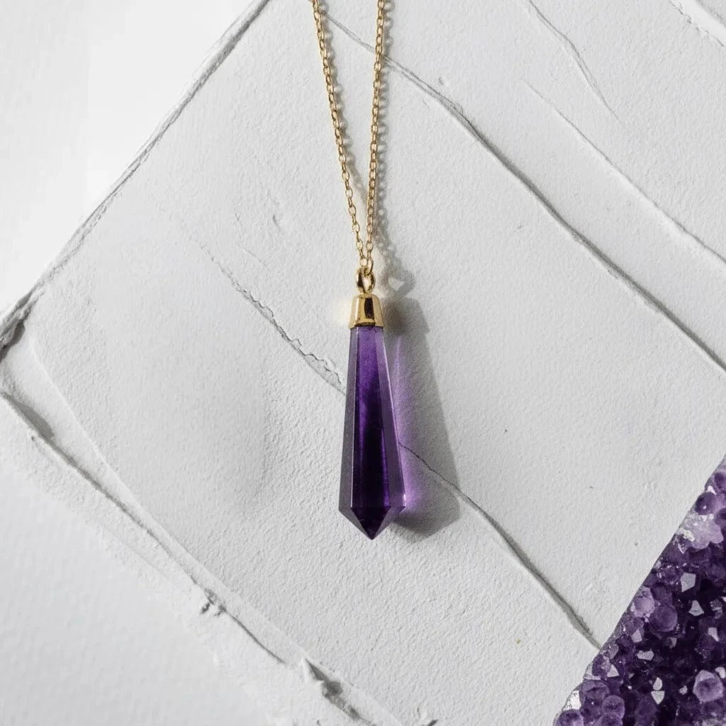 Purple crystal pendant necklace on a gold chain against a white marble background