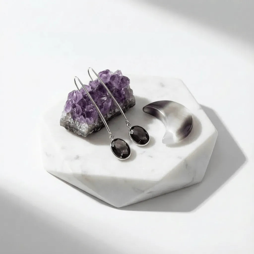 Silver earrings with purple stones on a white marble surface with amethyst crystal