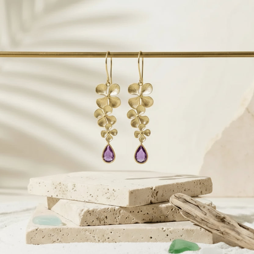 Gold earrings with blue stones on a stone surface with text 'Triple Orchid Earrings Cascading Plumeria in Gold & Capri'.