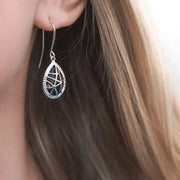 Close-up of a person wearing a silver teardrop earring with gemstones.