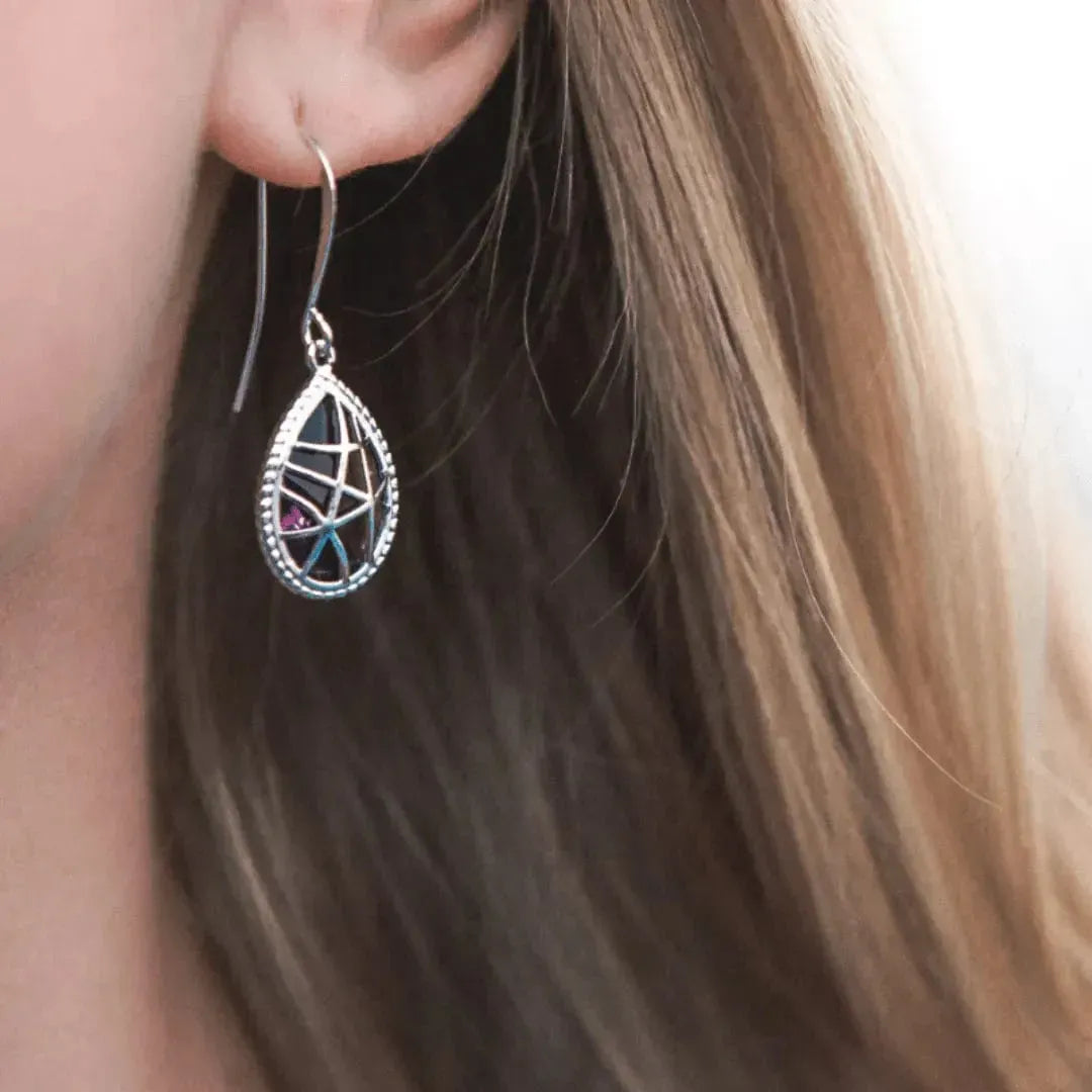Close-up of a person wearing a silver teardrop earring with gemstones.