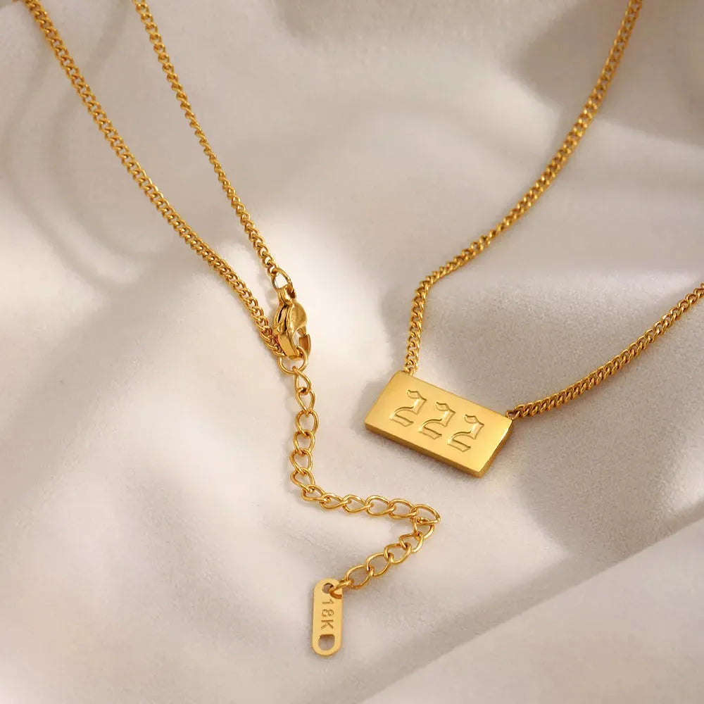 Two gold necklaces with engraved tags on a beige fabric background