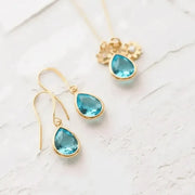 Gold earrings with blue teardrop stones on a light background
