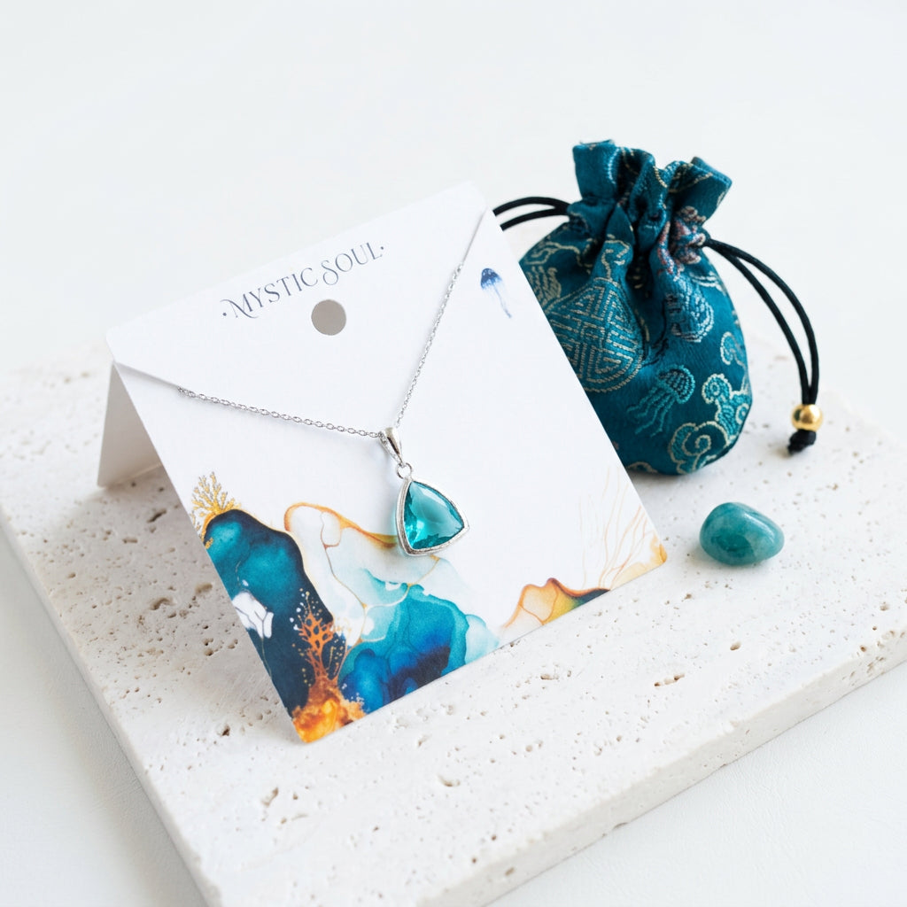 Silver Aqua Athena necklace with ocean blue faceted glass pendant, shown with gift tag and satin pouch, March birthstone colour