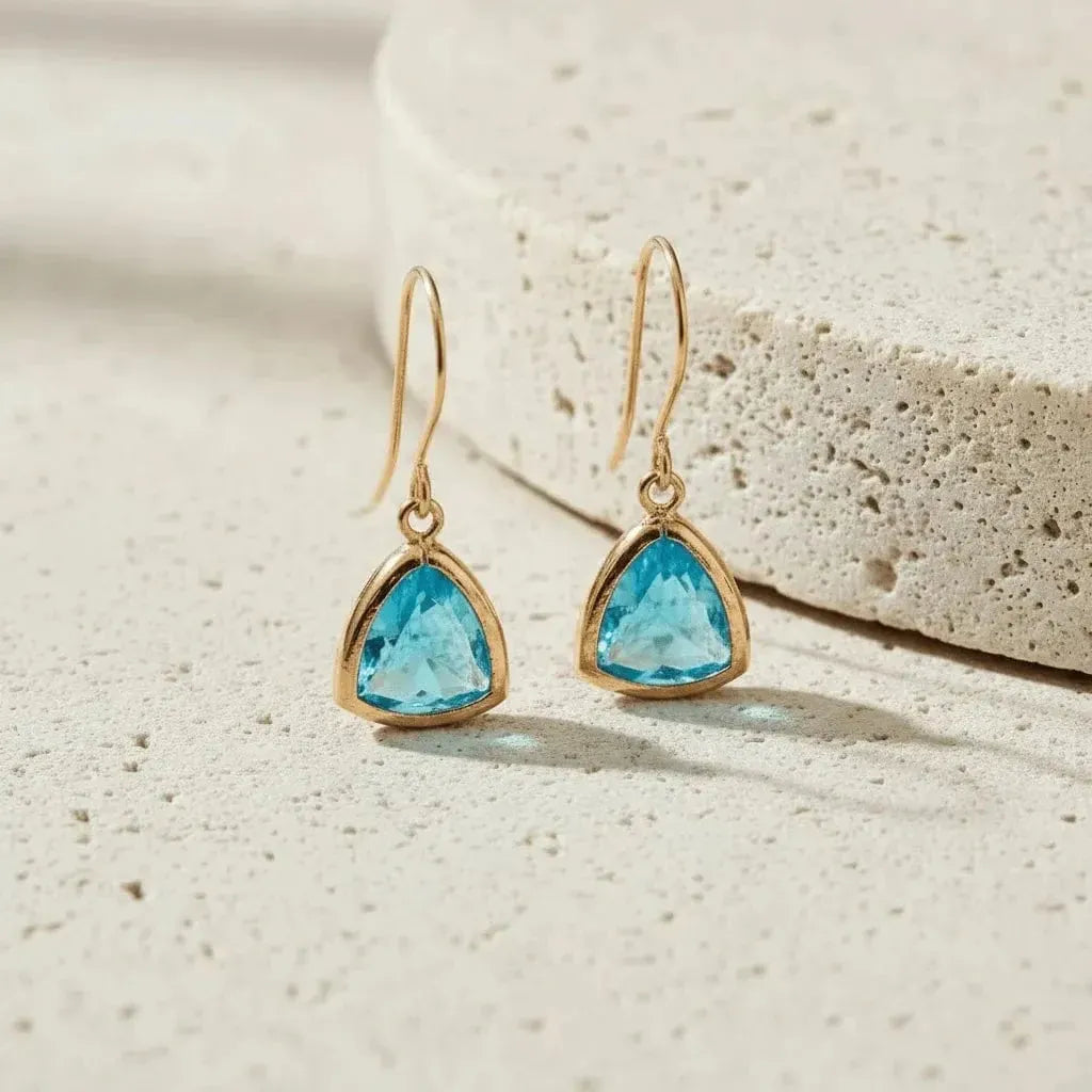 Gold earrings with blue gemstones on a textured beige surface