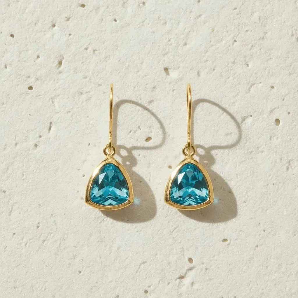 Gold earrings with blue gemstones on a textured beige background