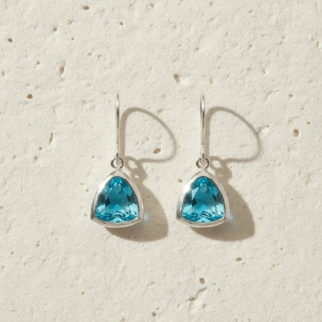 Teardrop-shaped blue gemstone earrings on a textured beige background