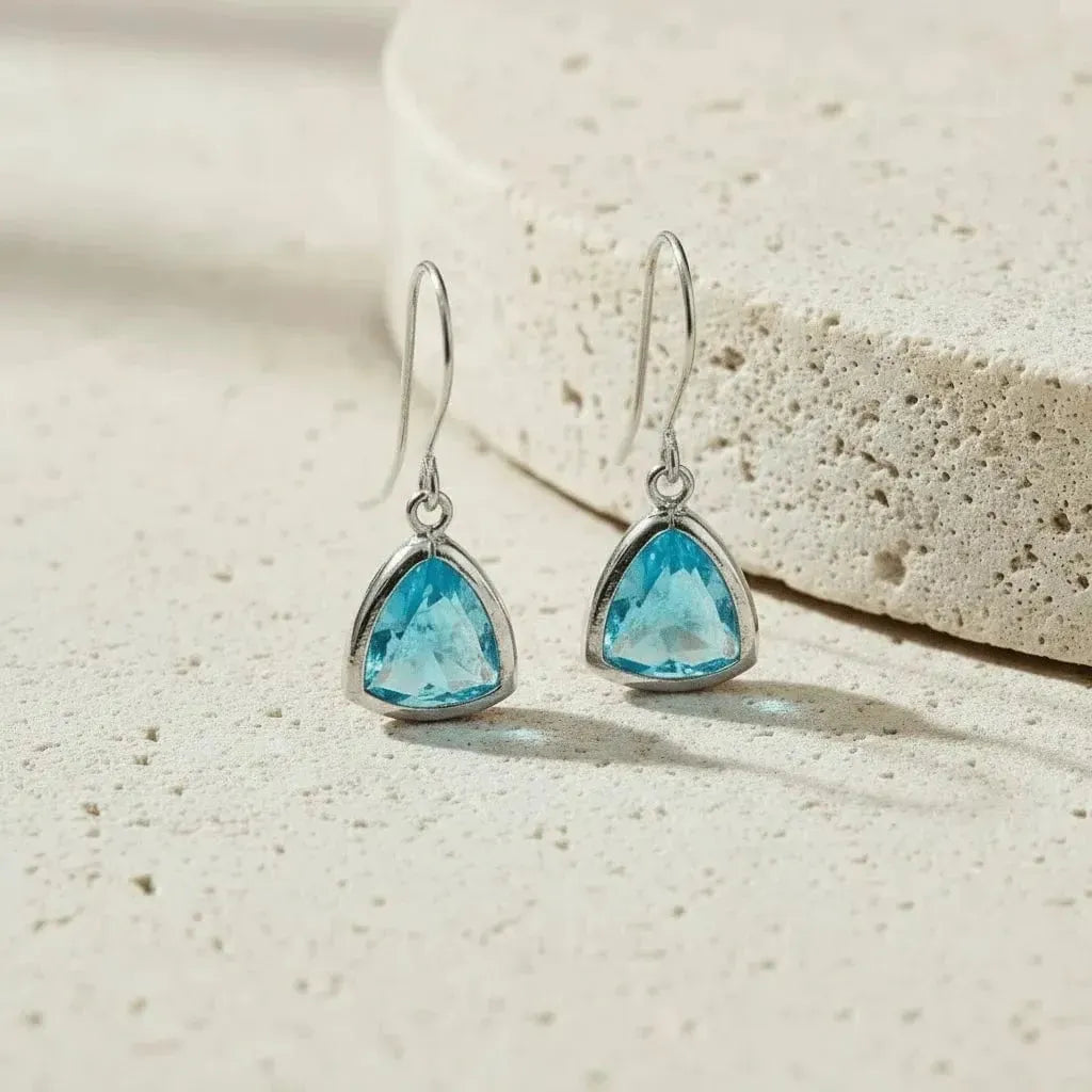 Pair of blue gemstone earrings on a beige stone background