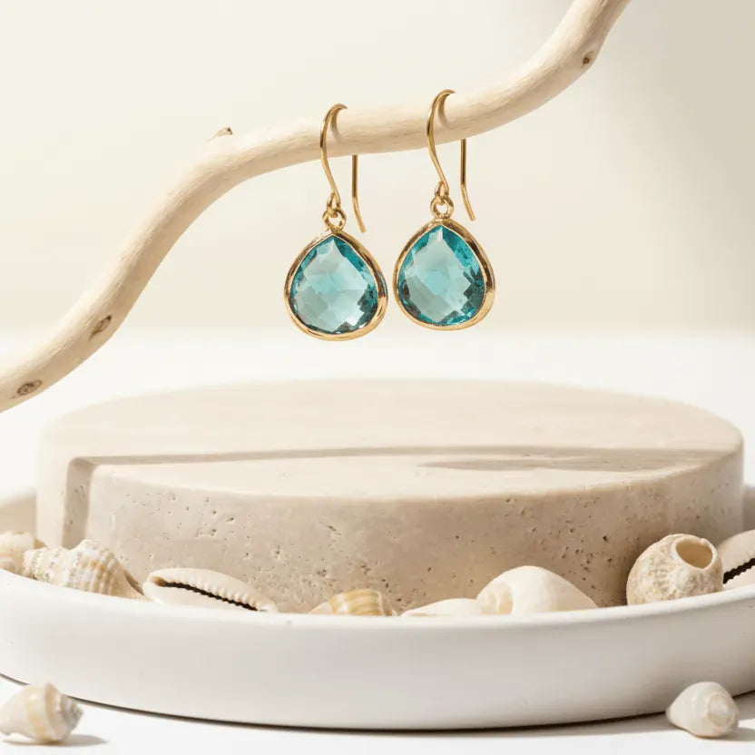 Gold earrings with blue gemstones on a natural wood and stone background