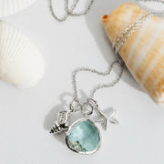 Necklace with a blue pendant and starfish charm on a white surface with shells.