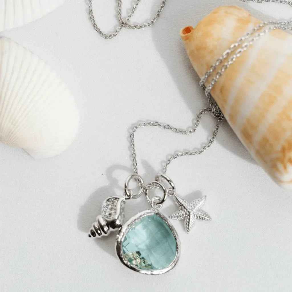 Necklace with a blue pendant and starfish charm on a white surface with shells.
