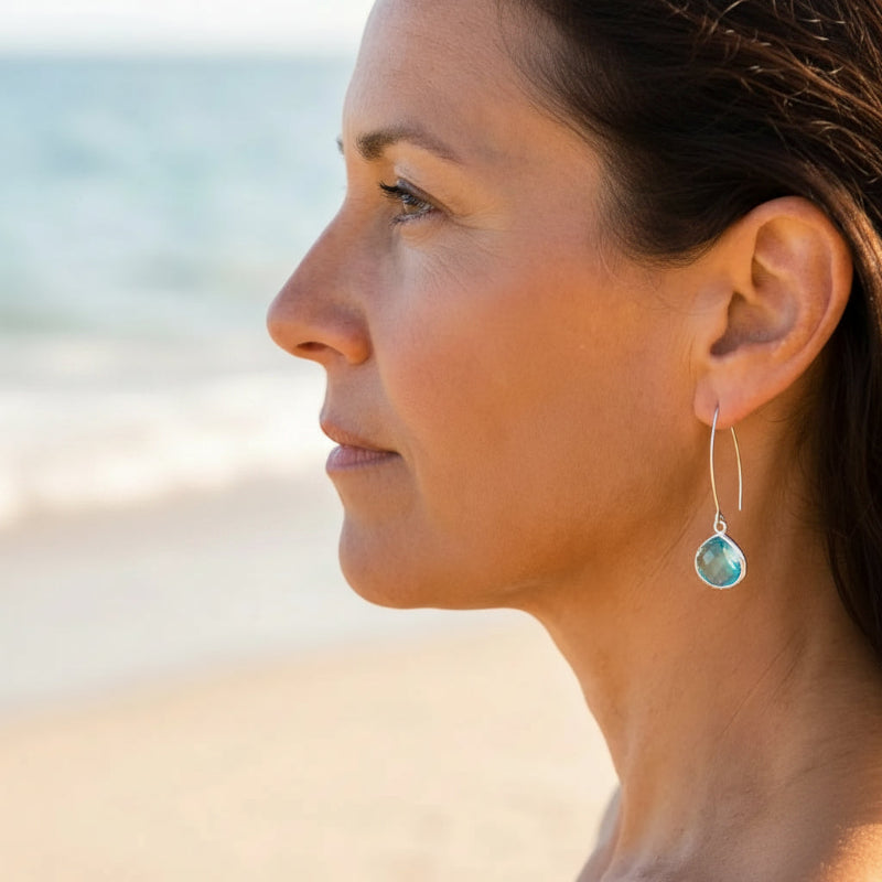 Woman on beach wearing aqua blue elegant earrings in silver, March birthstone jewelry
