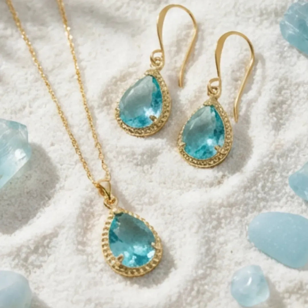 Gold jewelry set with blue teardrop stones on a textured white surface.