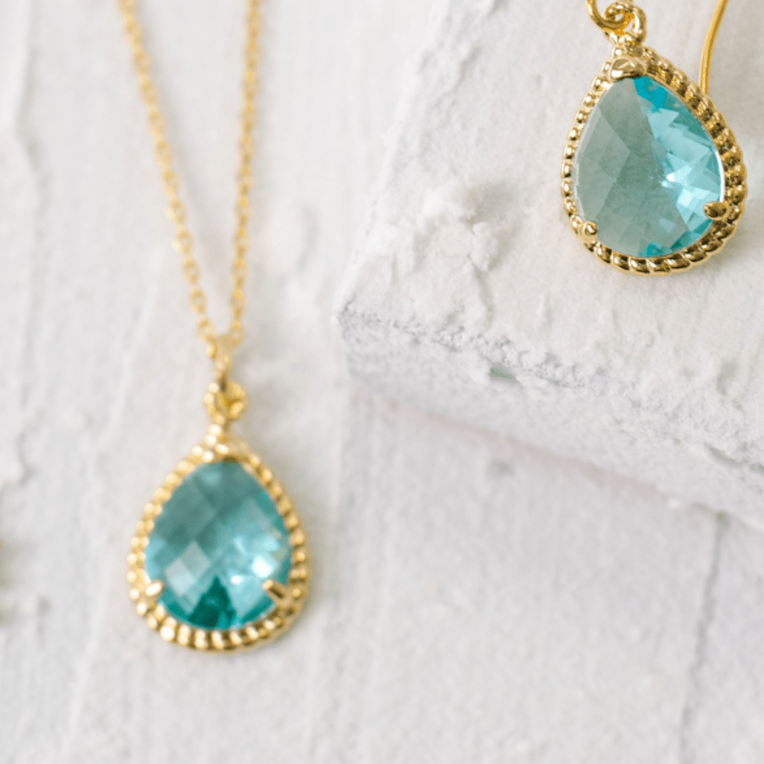 Teal teardrop earrings with gold accents on a white lace background