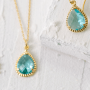 Teal teardrop earrings with gold accents on a white lace background