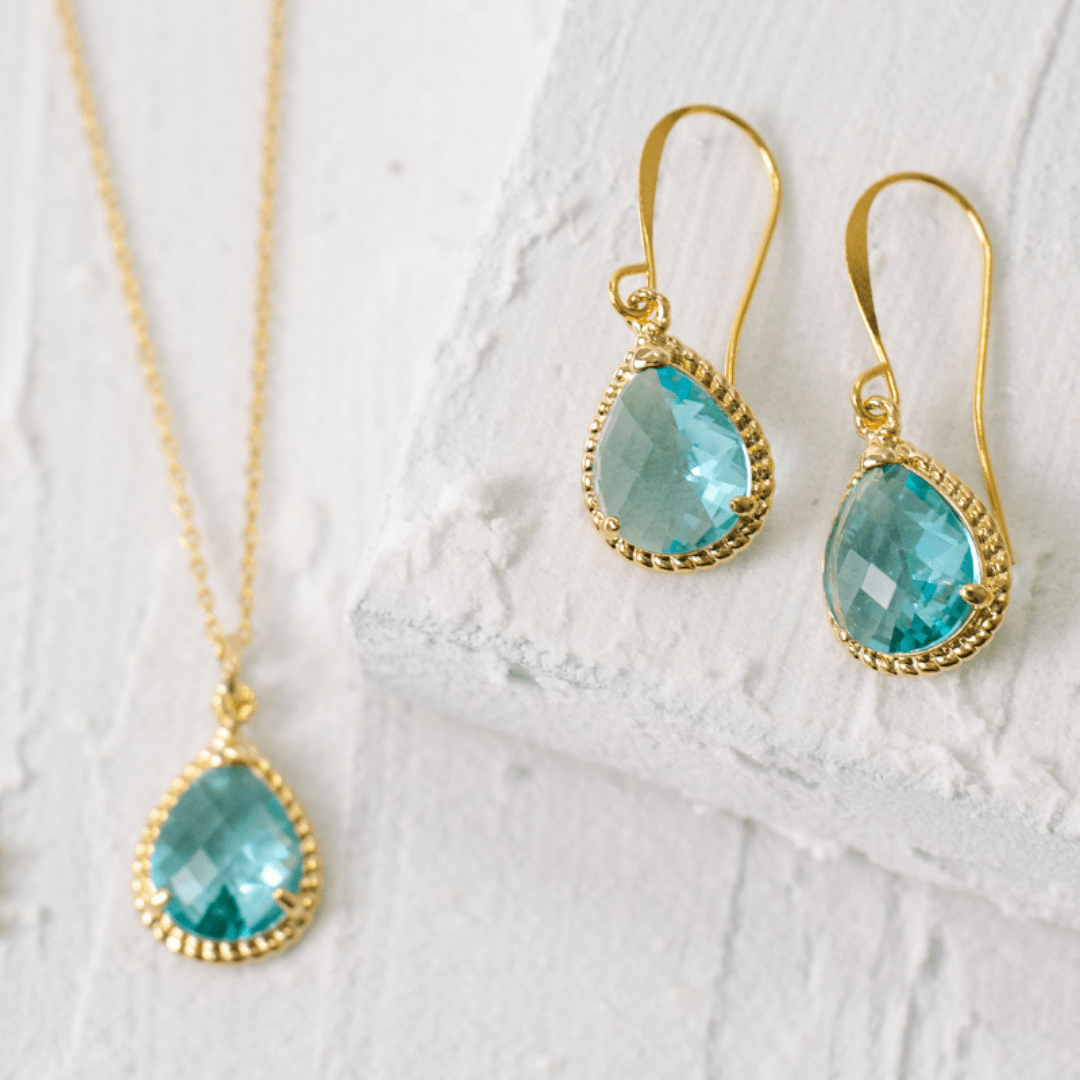 Gold-framed turquoise teardrop earrings on a white textured surface