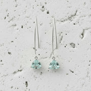 Pair of silver earrings with green gemstones on a textured gray background