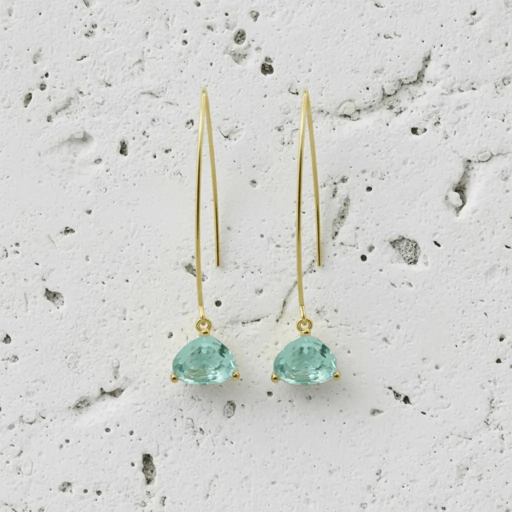 Gold earrings with green gemstones on a textured gray surface