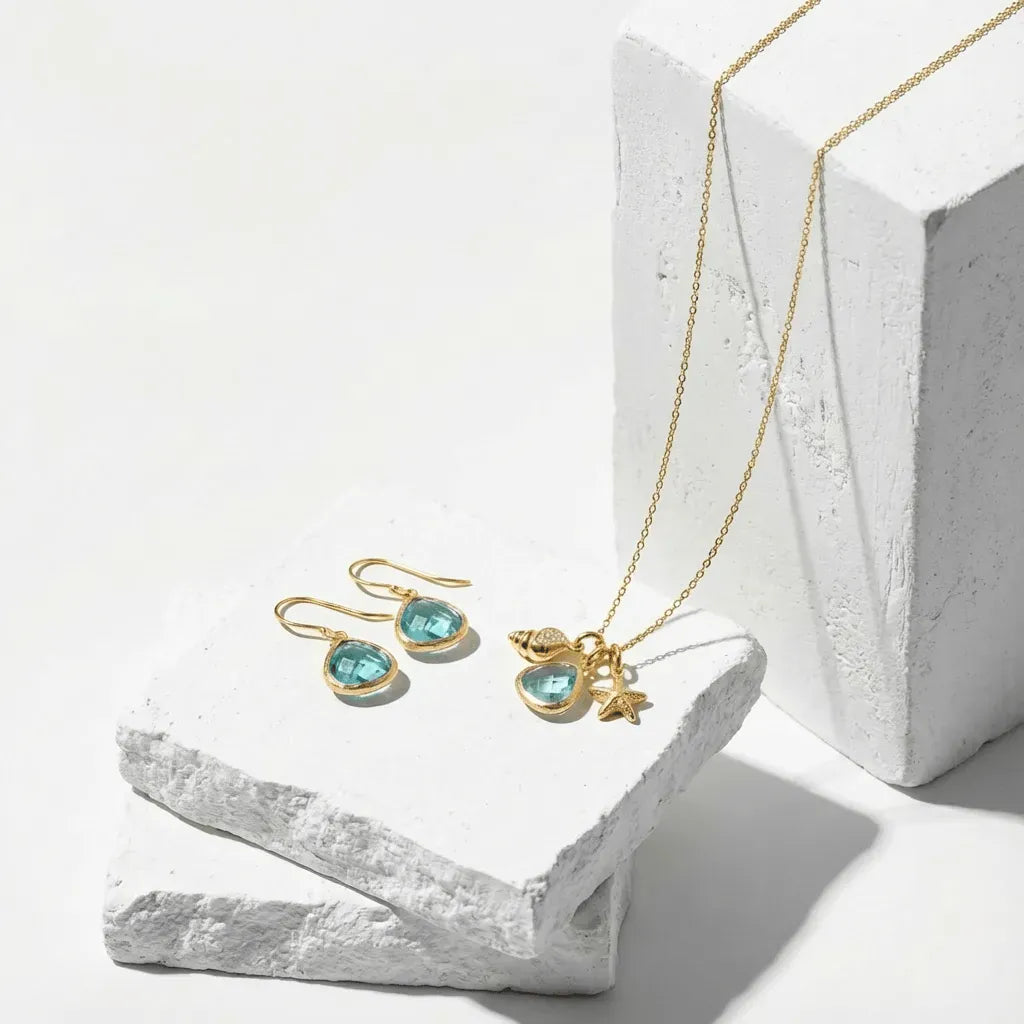 Gold necklace and earrings with blue gemstones on a white stone surface