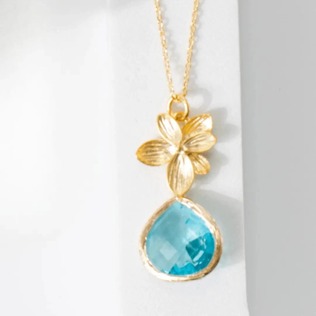 Gold necklace with a blue teardrop pendant on a white background