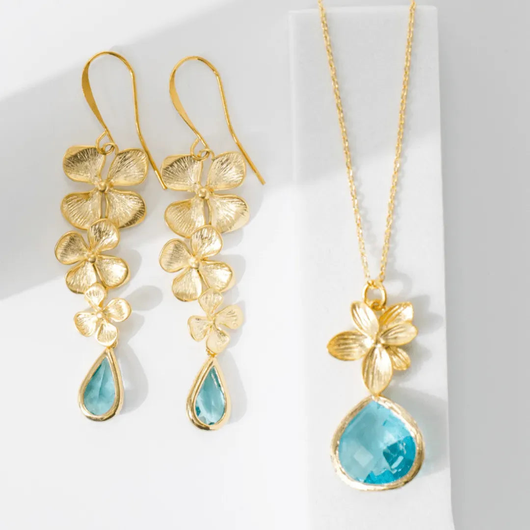 Gold floral earrings and necklace with blue teardrop stones on a white background