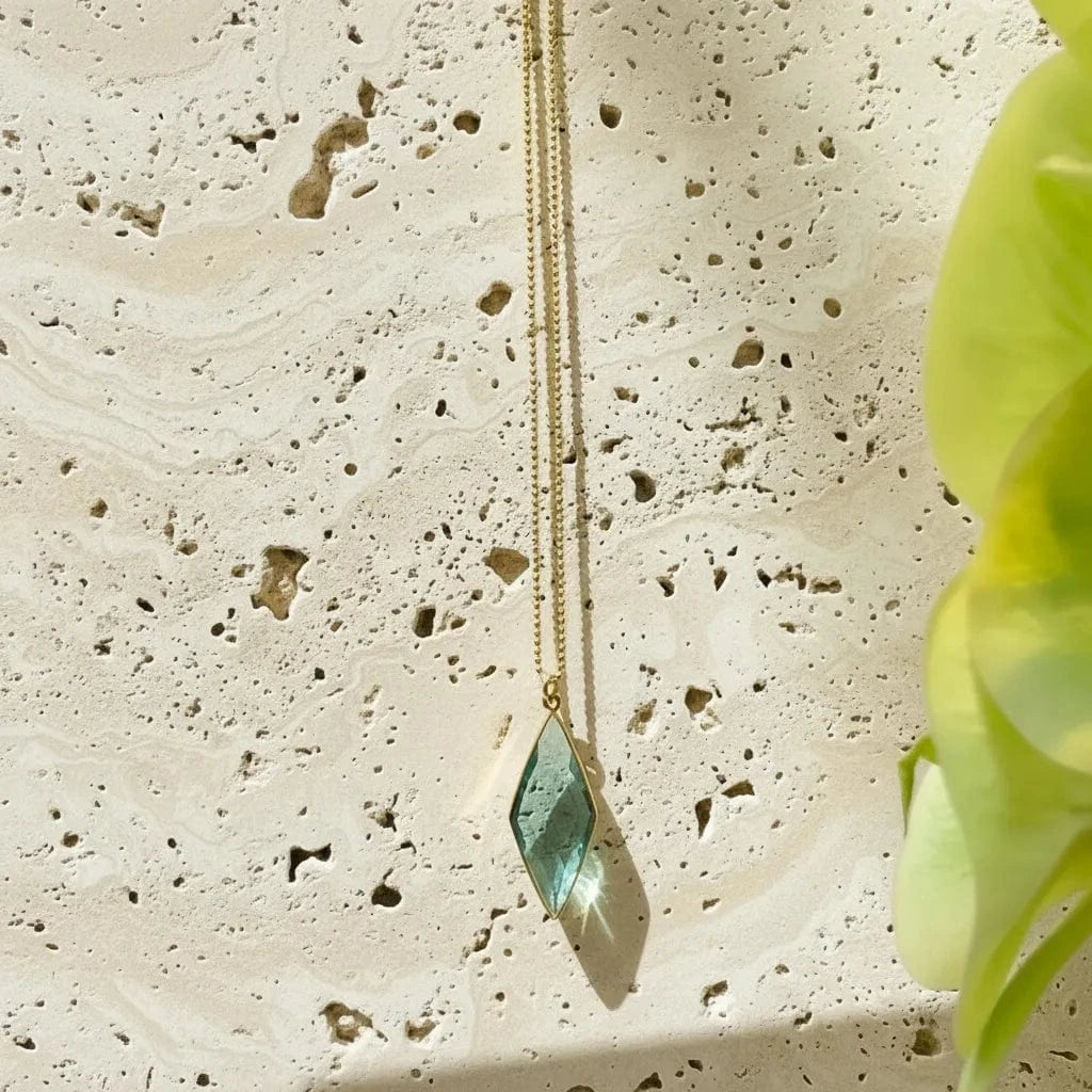 Gold necklace with a green pendant on a textured stone surface
