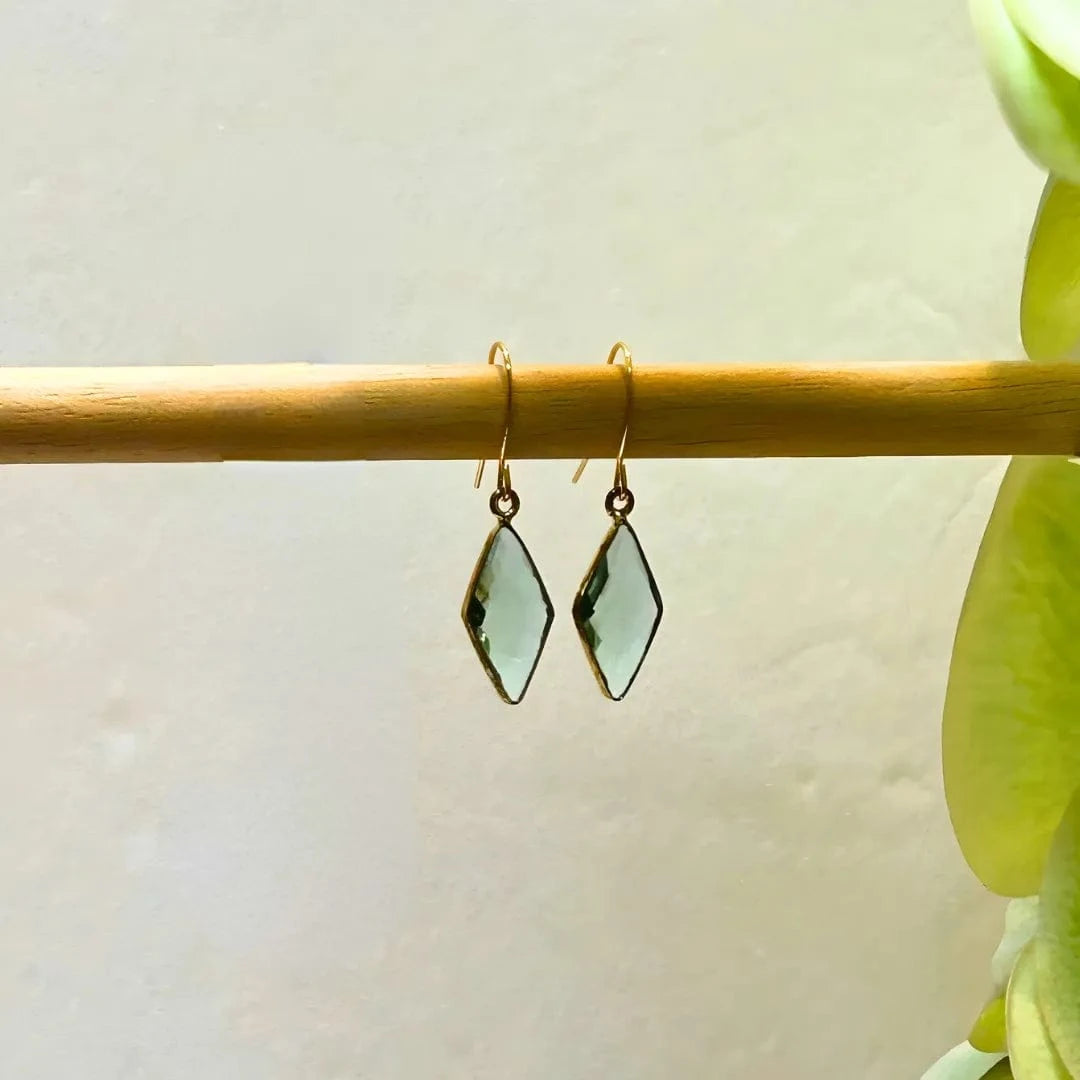 Pair of green earrings on a wooden stick with a light background
