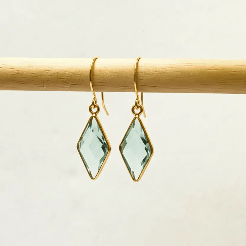 Gold earrings with green gemstones on a wooden stick against a beige background