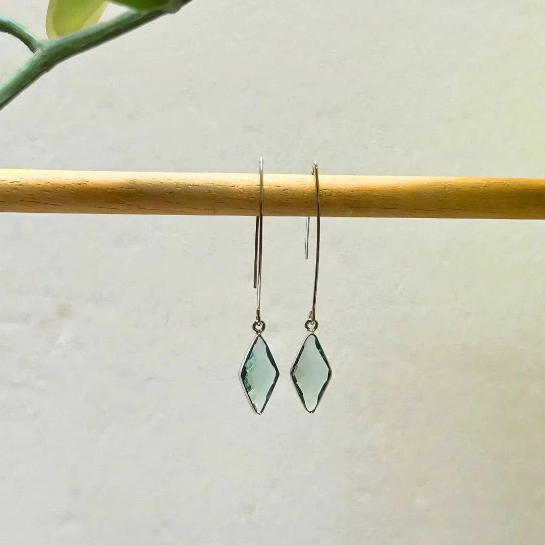 Pair of green gemstone earrings on a wooden stick with a light background