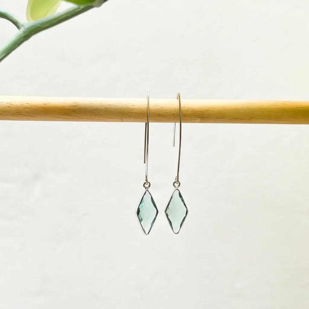 Pair of green gemstone earrings on a wooden stick with a light background
