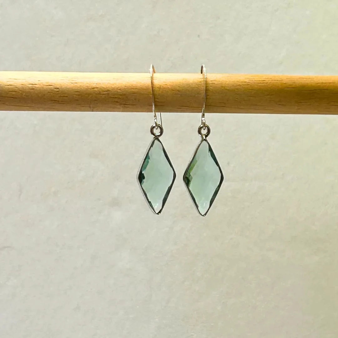 Green diamond-shaped earrings on a wooden rod against a light background