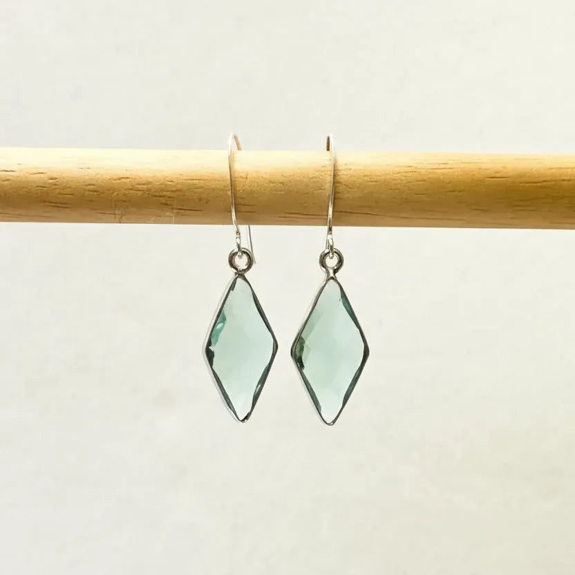 Green diamond-shaped earrings on a wooden rod against a light background