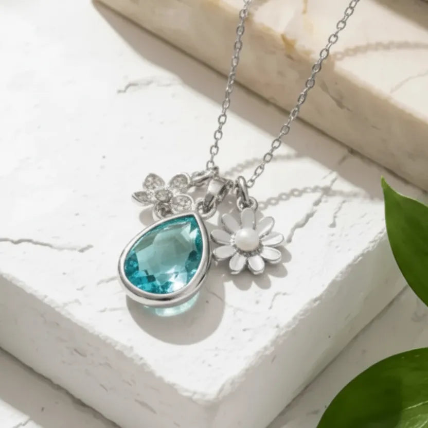 Necklace with blue teardrop pendant and white flower charm on a light background