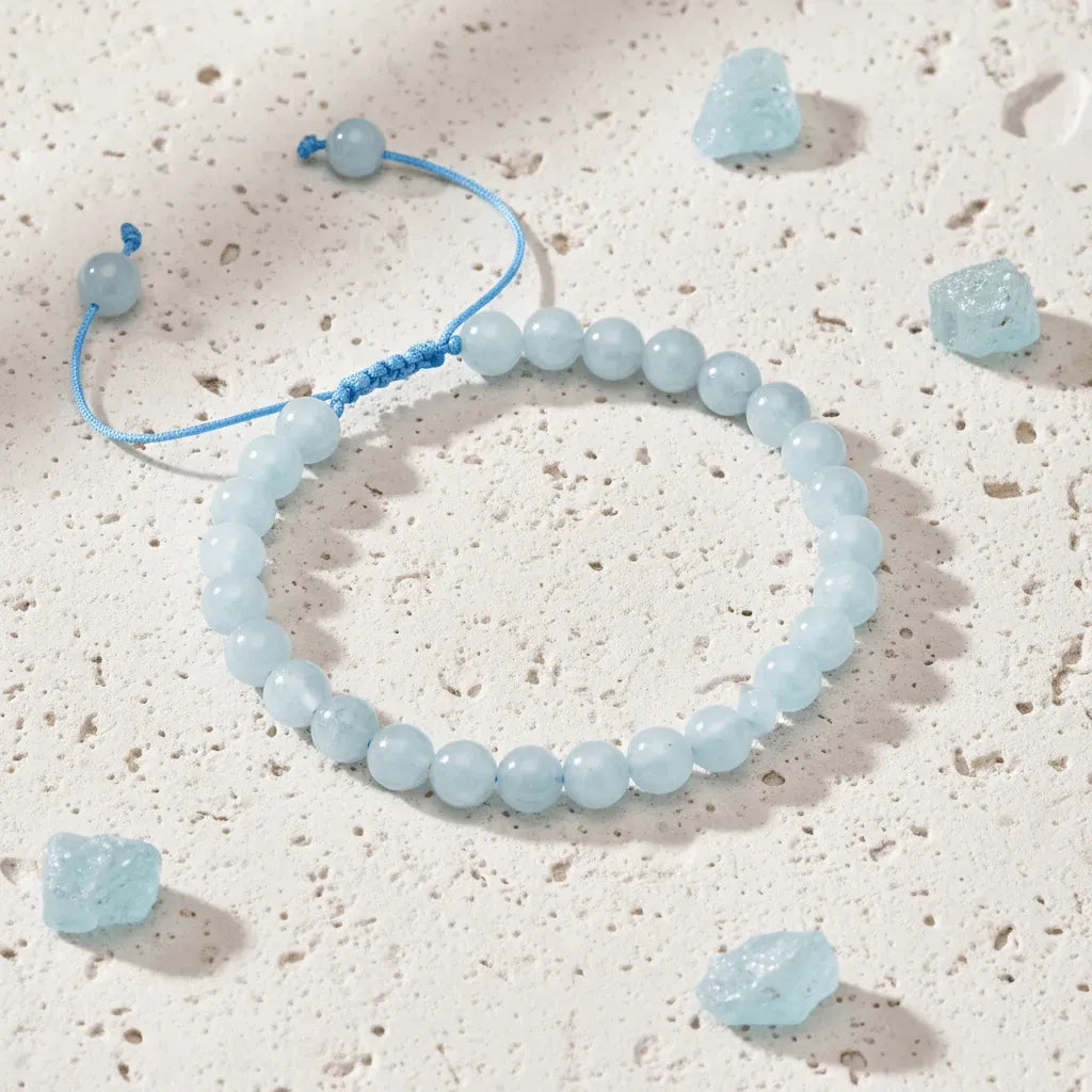 Blue beaded bracelet on a textured beige surface with scattered blue stones.